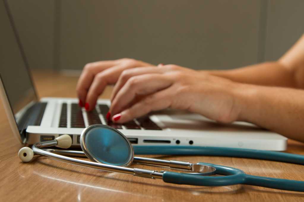 Woman on laptop keyboard with stethoscope nearby on desk