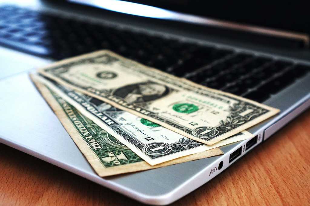 Laptop with black screen and three dollar bills laid out on keyboard