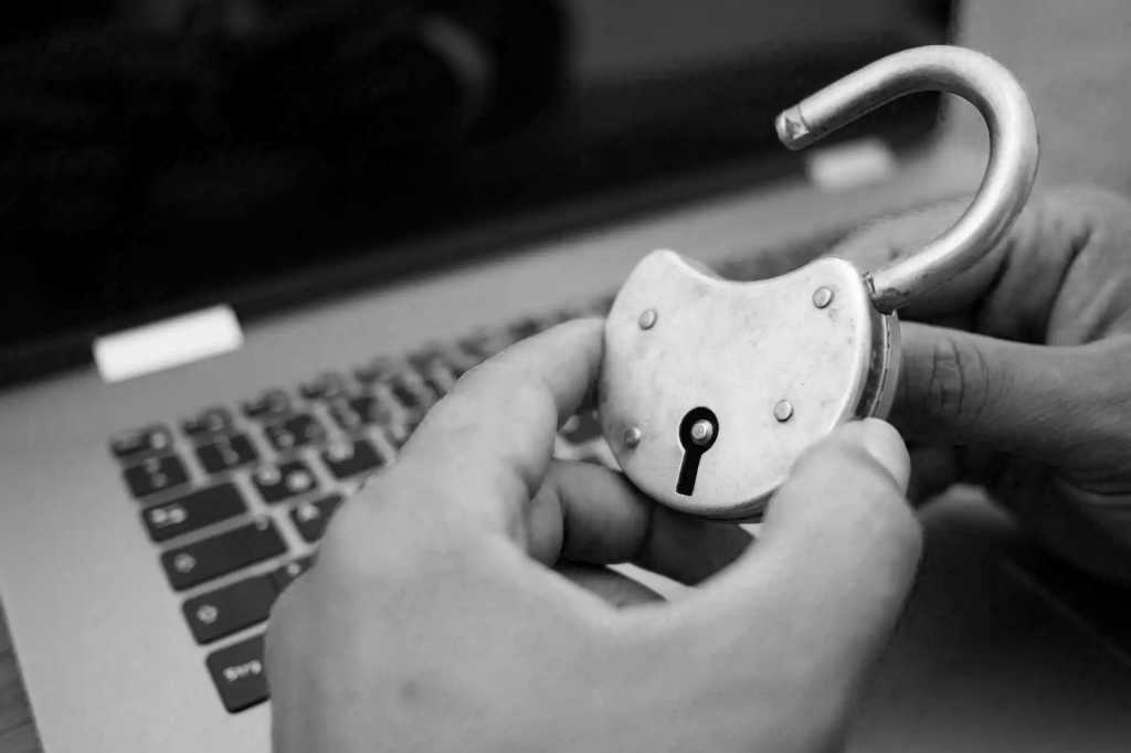 adult hands holding an open padlock in front of a laptop