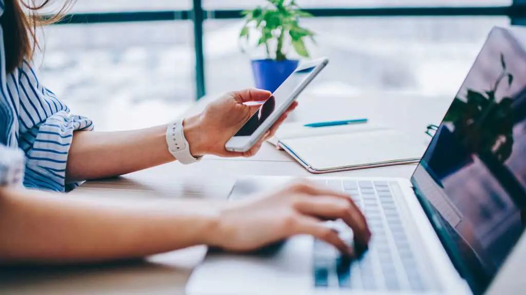 Woman with phone in one hand and laptop in the other