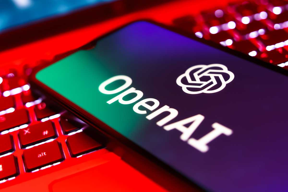 Logo OpenAI sur un écran de téléphone au-dessus d'un clavier d'ordinateur portable ouvert