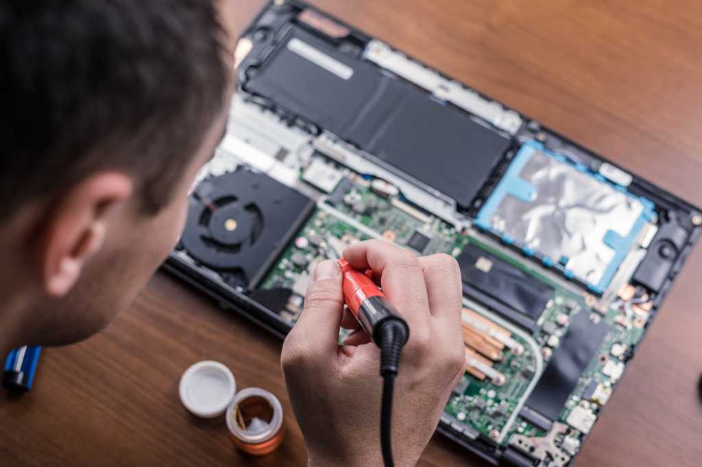 Man soldering an open laptop with internal components exposed