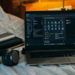 Laptop headphones accessories on bed in dorm room