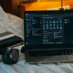 Laptop headphones accessories on bed in dorm room