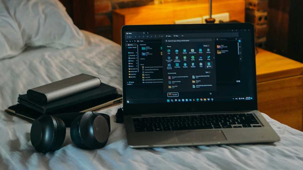 Laptop headphones accessories on bed in dorm room