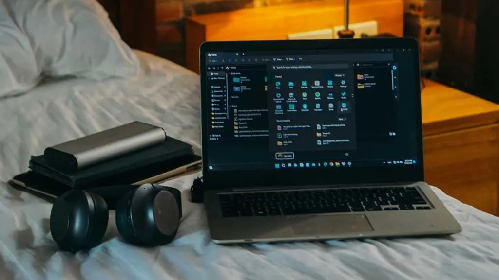 Laptop headphones accessories on bed in dorm room