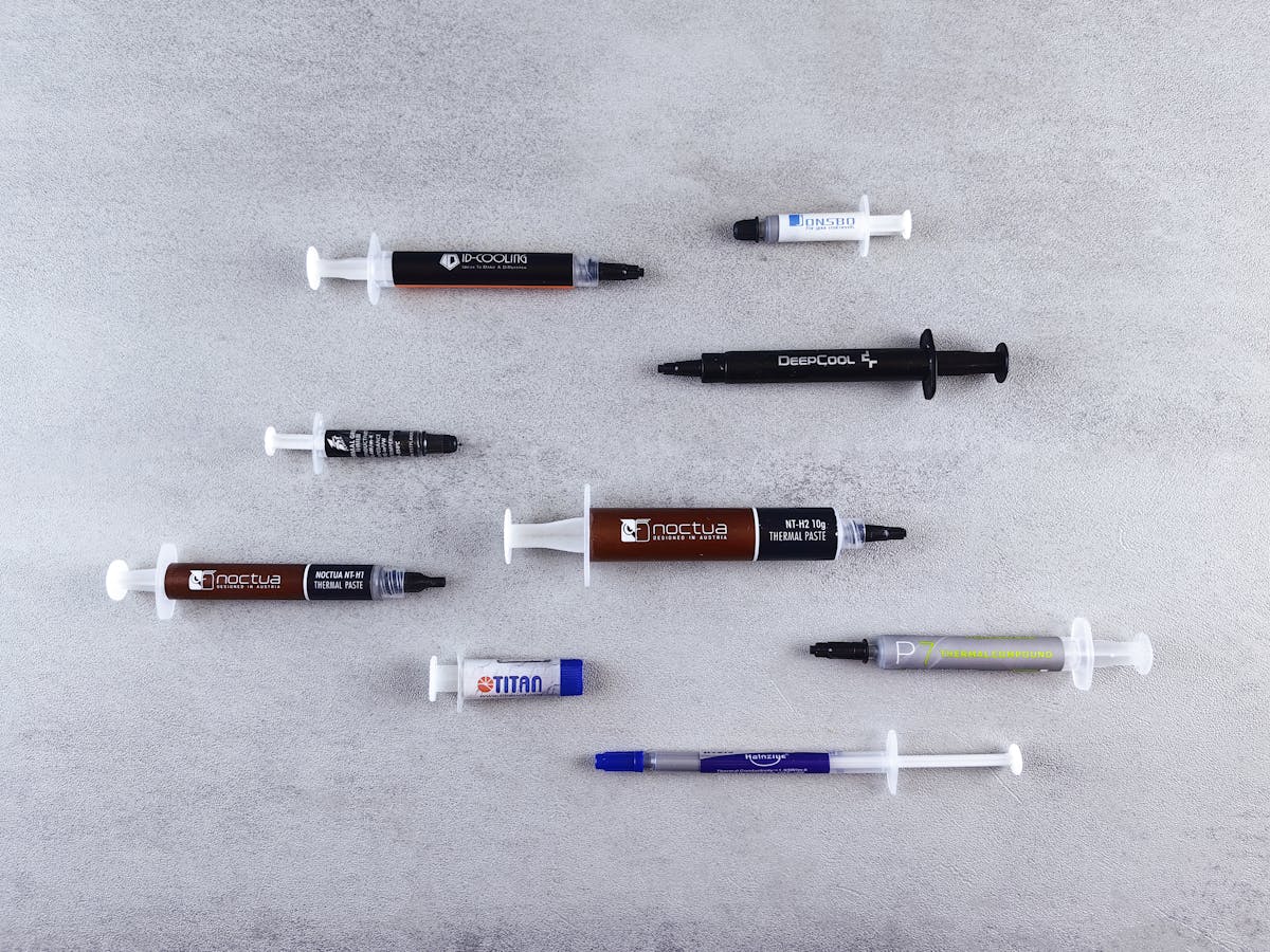 Flat lay of different thermal paste syringes on textured surface for computer hardware.