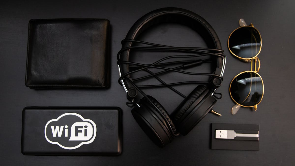 A stylish arrangement of essential accessories including headphones, wallet, and sunglasses on a black surface.