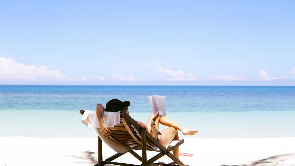 Person reading on a beach in a lounge chair