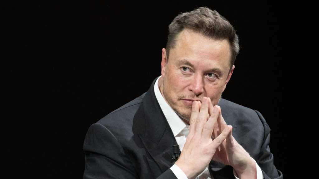 Elon Musk sitzend vor schwarzem Hintergrund