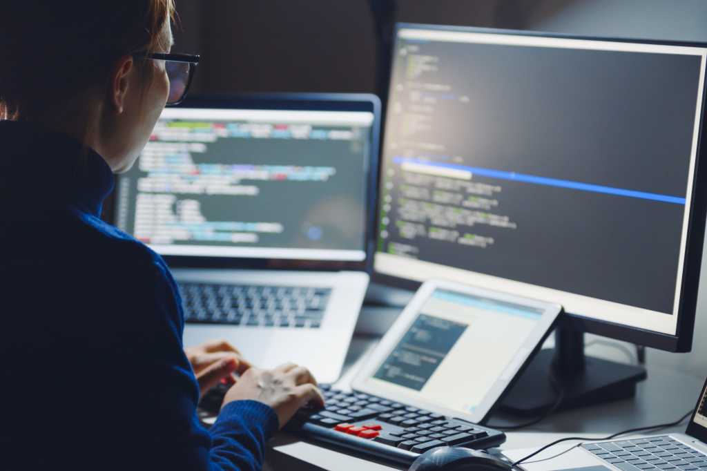 Woman in glasses coding with laptop monitor and tablet