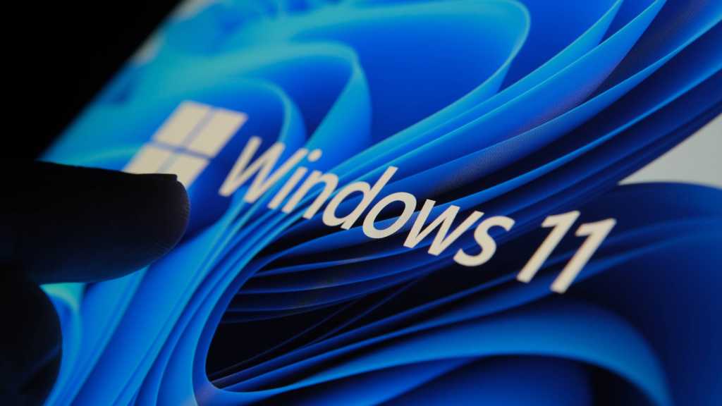 Finger touching Windows 11 logo on screen in dark room
