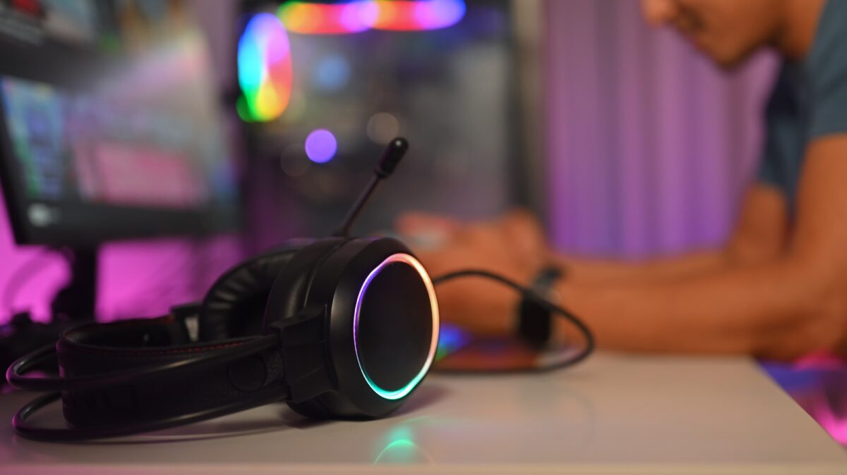 Gros plan sur un casque d'écoute posé sur un bureau avec un joueur assis à l'arrière-plan. Concept de jeu et de technologie