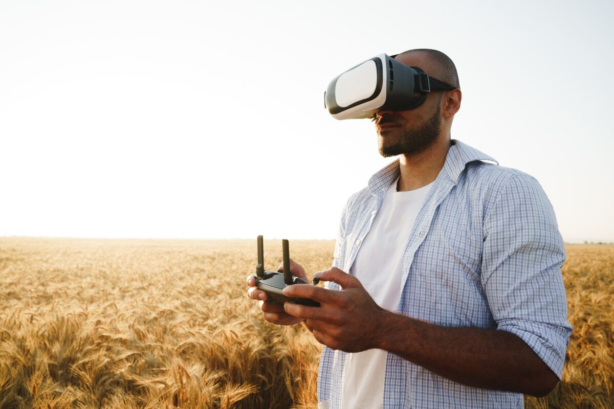 Young man standing in a wheat field at sunset in virtual reality glasses